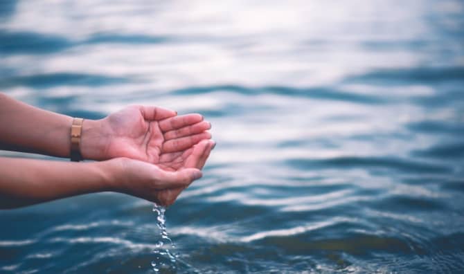 Two hands touch blue water.