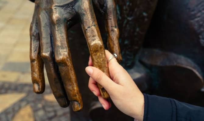 A visually impaired woman feels the hand of a bronze sculpture.