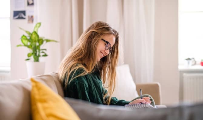 A woman smiling while writing on the couch.