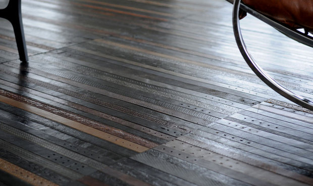 Close-up of wet hardwood flooring with visible wood grain patterns and reflections, with furniture visible at the top of the frame.