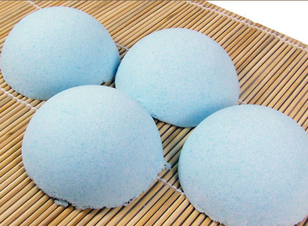 Four round blue bath bombs arranged on a bamboo mat, viewed from above.