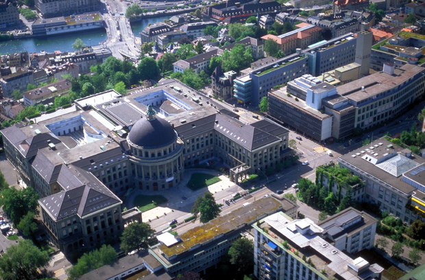 ETH Zurich, Aerial view of a city with a large domed governmental building, mixed historic and modern architecture, green spaces, and a waterway running through the urban landscape