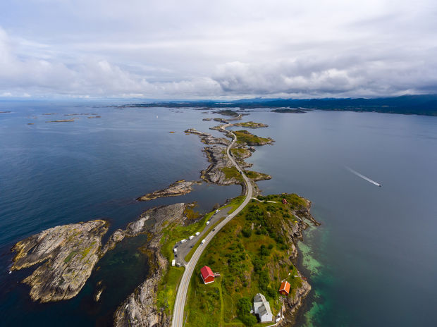 Aerial view of winding coastal road connecting small islands with red-roofed buildings surrounded by blue water and rocky terrain.