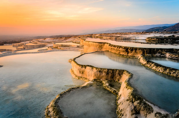 White limestone terraces with mineral pools filled with water, captured during golden hour with warm sunset lighting.