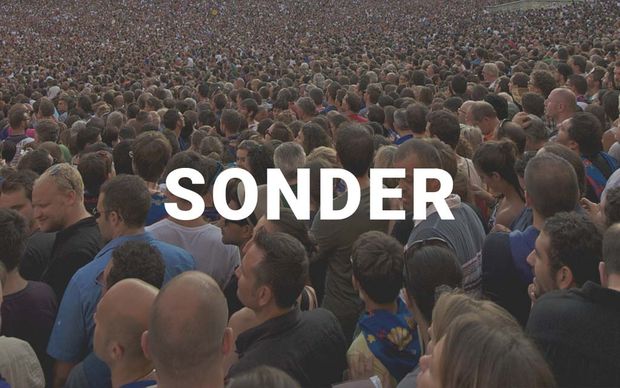 An aerial view of a massive, densely packed crowd of people with the word 'SONDER' displayed in large white capital letters across the center of the image.