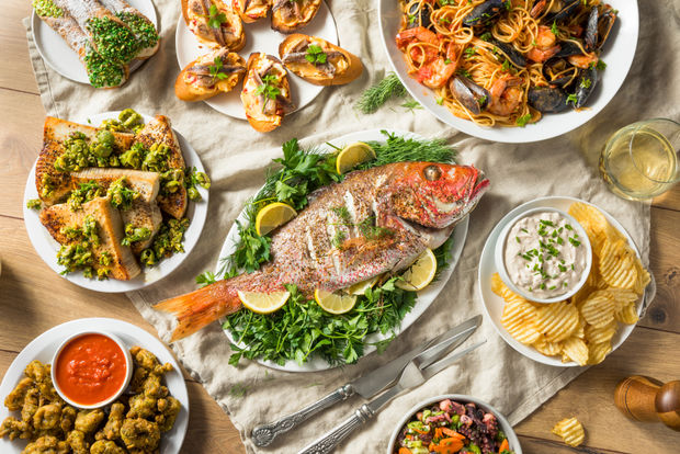 Mediterranean seafood spread with grilled whole fish, shrimp dishes, calamari, flatbread appetizers, dips, and lemon garnishes on white plates and wooden surface.