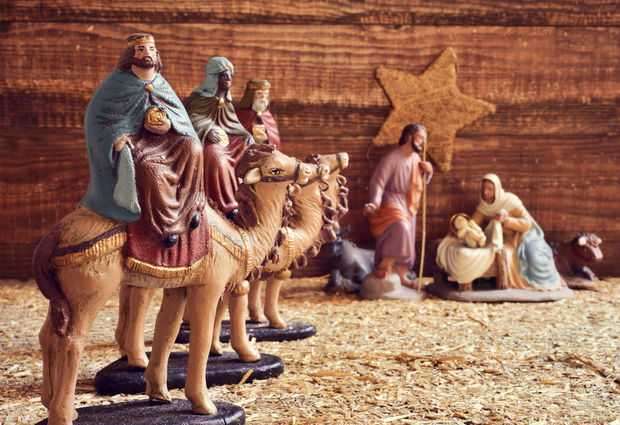 Nativity scene with three wise men figurines on camels, Jesus, Mary, Joseph, and shepherds on sand with a golden star in the background.