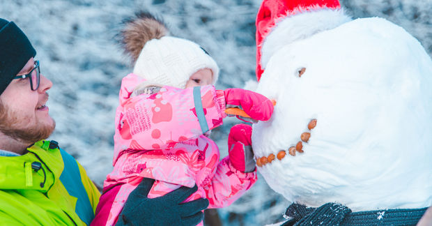 Father and child building snowman outdoors.
