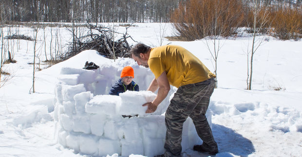 Father and child building snow fort outdoors.