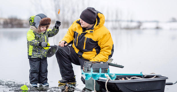 Father and child ice fishing on frozen lake.