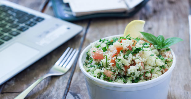 a bowle of salad on a wooden table with a laptop in the back round