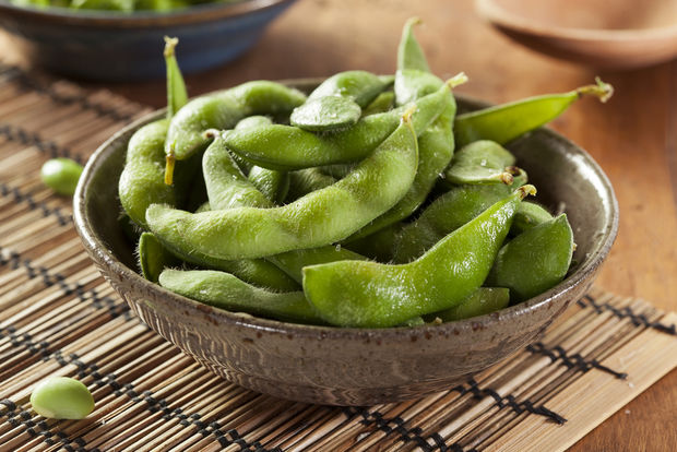 A rustic ceramic bowl filled with steamed edamame pods, served on a bamboo placemat on a wooden table