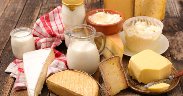 An assortment of dairy products including milk, butter, various cheeses, and cottage cheese on a rustic wooden table.