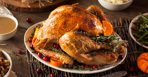 A golden roasted turkey garnished with rosemary, cranberries, and orange slices on a platter with side dishes nearby.