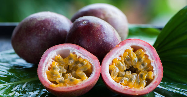 Fresh passion fruits, one cut in half revealing golden seedy pulp, displayed on a green tropical leaf outdoors.