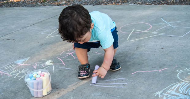 photo Child drawing with colorful chalk on pavement.