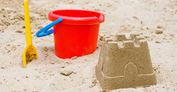 photo Red bucket and yellow shovel with sand castle.