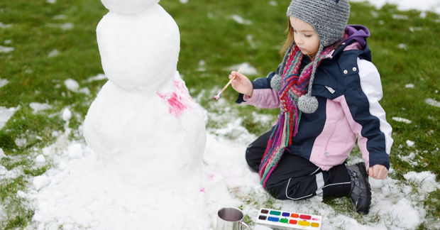 Child painting snowman with colorful paints outdoors.