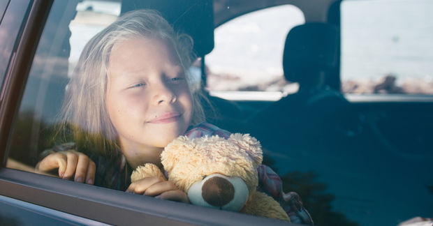 girl looking through the window holding a teddybear