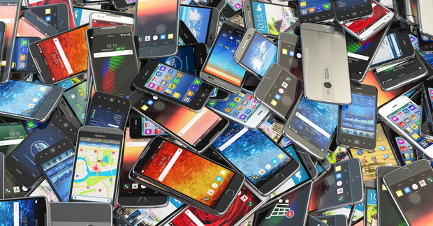 A large pile of various smartphones with colorful screens, different brands and sizes, stacked haphazardly together.