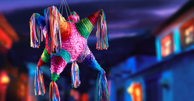 Colorful star-shaped piñata with rainbow colors and tissue paper fringe hanging in front of blurred festive bokeh background.