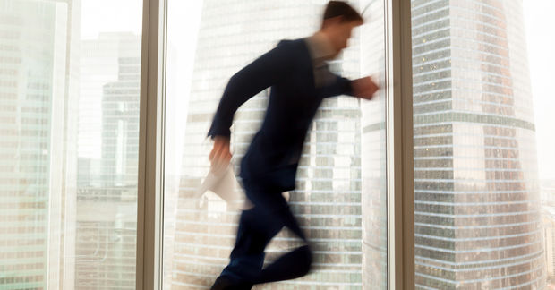 photo Blurred figure of person running through modern office building with large windows, motion blur suggesting speed and urgency.