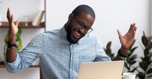 man looks happy raising hands infront of a laptop