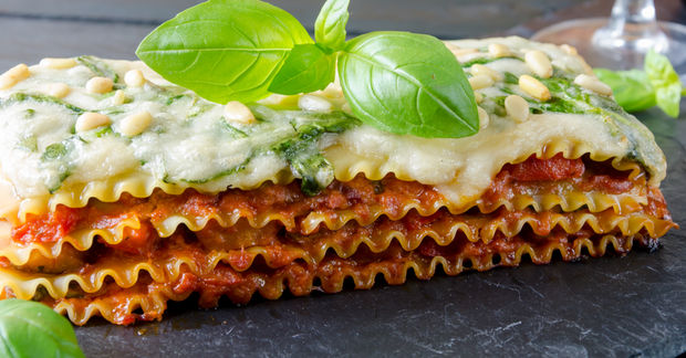 Layered lasagna slice topped with fresh basil leaves.