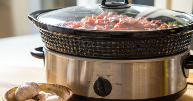 Slow cooker with meat stew and garlic cloves.