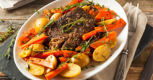 Roasted beef with vegetables and herbs on platter.