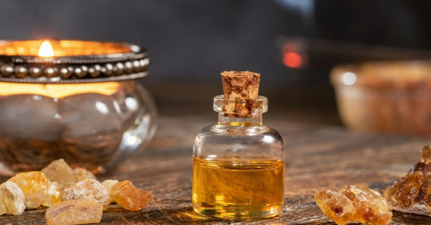 photo A small corked glass bottle of golden essential oil surrounded by frankincense resin and a glowing candle in the background.