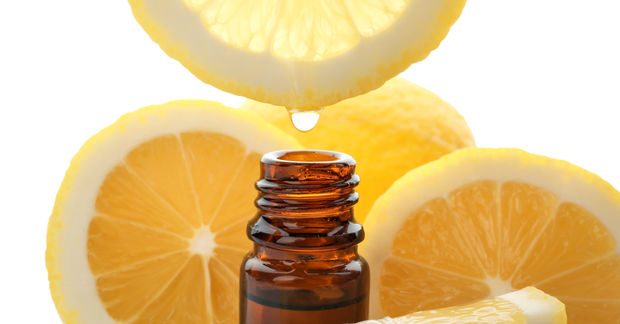 photo A drop of lemon juice falls from a squeezed lemon half into a small brown essential oil bottle, surrounded by lemon slices.