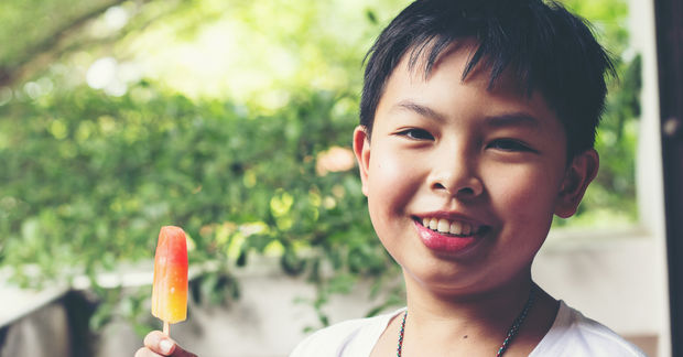 Happy boy eating colorful popsicle outdoors.