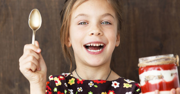 Happy girl with spoon and layered dessert jar.