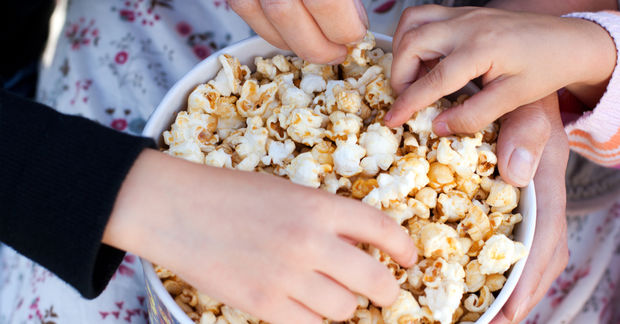Hands reaching for popcorn in bowl.
