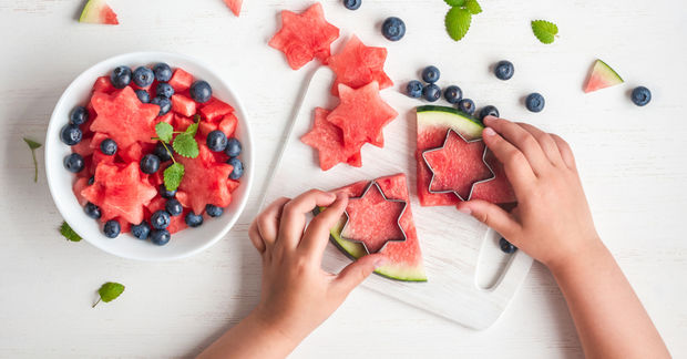 Hands cutting star-shaped watermelon with blueberry bowl.