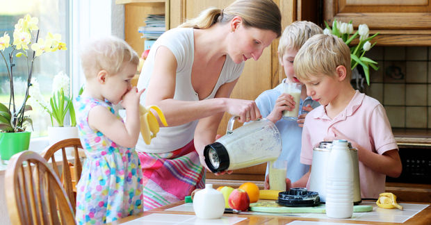 Mother preparing breakfast with two children in kitchen.