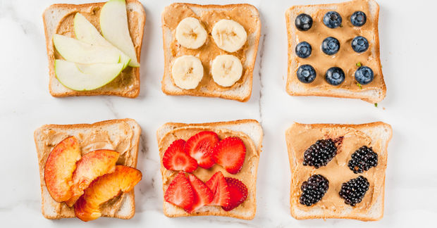 Six slices of buttered whole wheat toast arranged in a grid, each topped with different fresh fruits: apple slices, banana, blueberries, peach slices, strawberries, and blackberries.
