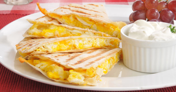 Cheese quesadillas cut into triangles on a white plate served with sour cream dip and red grapes.