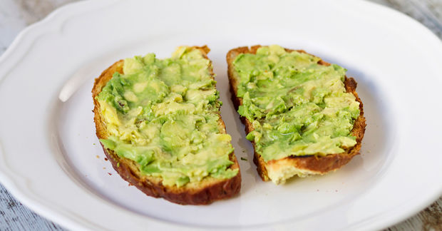Two slices of toasted bread topped with mashed avocado on a white plate.