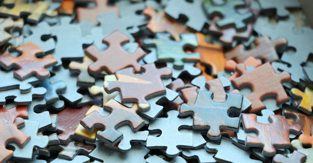 Puzzles Scattered colorful puzzle pieces in blue, pink, orange, and yellow scattered across a light blue surface in shallow focus.