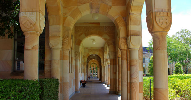 The University of Queenland, Long stone colonnade with arched ceiling and decorative columns, with ivy on the sides and bright daylight at the end of the corridor.