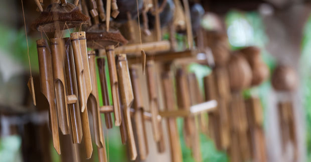 Multiple handcrafted bamboo wind chimes hanging in a row with a soft-focus green background.